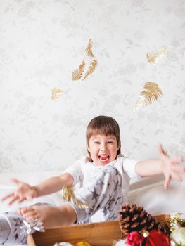 Joyful boy is playing with decorations for Christmas tree. Funny kid is ready for New Year celebration. Cozy home. Winter holiday spirit.