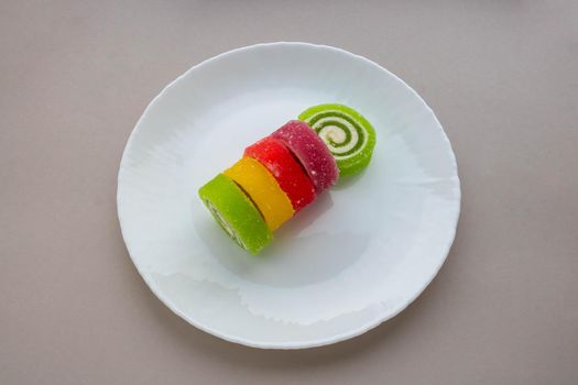 Multicolored spiral marmalade on a white plate on a gray background.