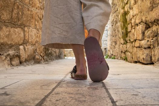 Detail shot of female legs wearing comfortable travel sandals walking on old medieval cobblestones street dring sightseeing city tour. Travel, tourism, and adventure concept.