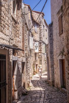 Rear view of beautiful blonde young female traveler wearing straw sun hat sightseeing and enjoying summer vacation in an old traditional costal town at Adriatic cost, Croatia.