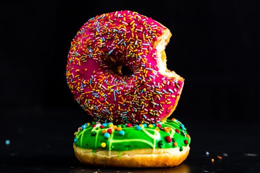 Bitten pink glazed donut with sprinkles isolated. Close up of colorful donuts.