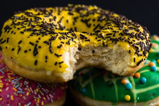 Bitten yellow glazed donut with sprinkles isolated. Close up of colorful donuts.