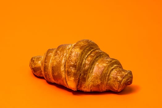 Fresh croissant isolated on orange board. French breakfast concept.