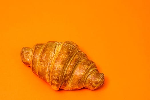 Fresh croissant isolated on orange board. French breakfast concept.