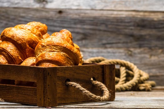 Wooden crate with delicious, fresh croissants isolated. French breakfast concept.