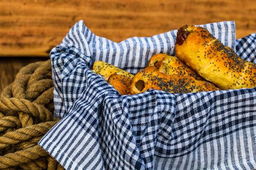 Sausages baked in dough sprinkled with salt and poppy seeds in a rustic composition. Sausages rolls, delicious homemade pastries.