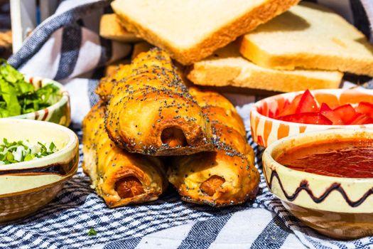 Sausages baked in dough sprinkled with salt and poppy seeds in a rustic composition. Sausages rolls, delicious homemade pastries.