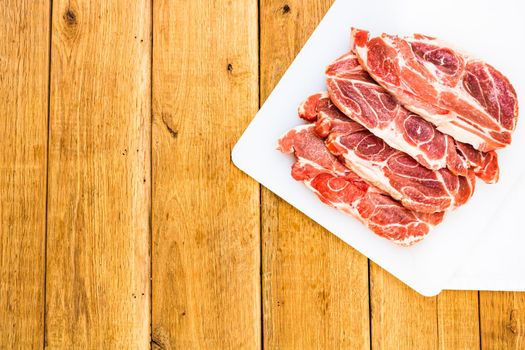 Pork chops on a white cutting board over wooden table, meat for bbq, top view, copy space, barbeque concept