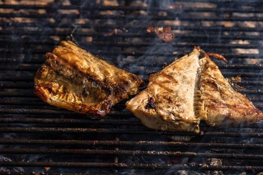 Grilled mackerel fish with smoke on a charcoal barbecue grill.