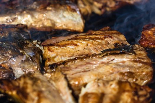 Grilled mackerel fish with smoke on a charcoal barbecue grill.