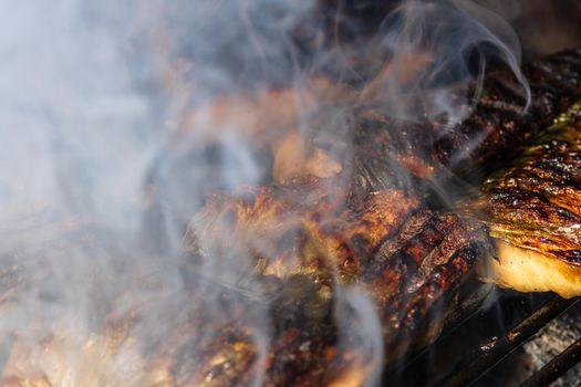 Grilled mackerel fish with smoke on a charcoal barbecue grill.