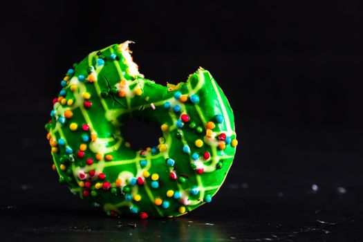 Green glazed donut with sprinkles isolated. Close up of colorful bitten donut.