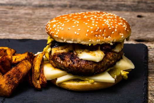 Detail view of fresh tasty cheese burger and fried potatoes on a wooden table