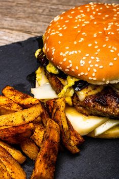 Detail view of fresh tasty cheese burger and fried potatoes on a wooden table