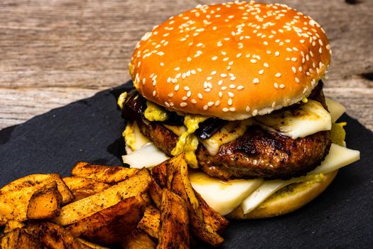 Homemade fresh tasty cheese burger and fried potatoes on a wooden table