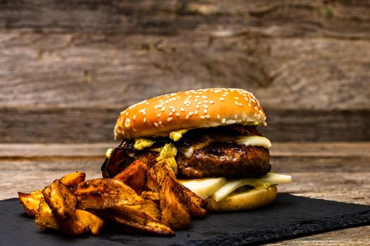 Homemade fresh tasty cheese burger and fried potatoes on a wooden table