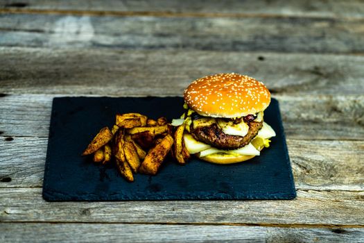 Homemade fresh tasty cheese burger and fried potatoes on a wooden table