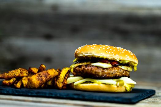 Homemade fresh tasty cheese burger and fried potatoes on a wooden table