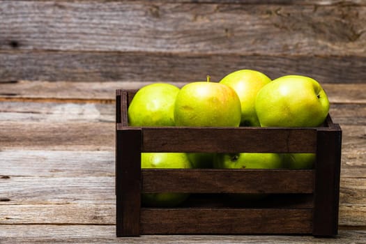 Wooden crate with ripe green apples on wooden table.