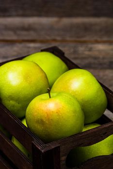 Wooden crate with ripe green apples on wooden table.