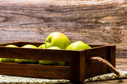 Wooden crate with ripe green apples on wooden table.