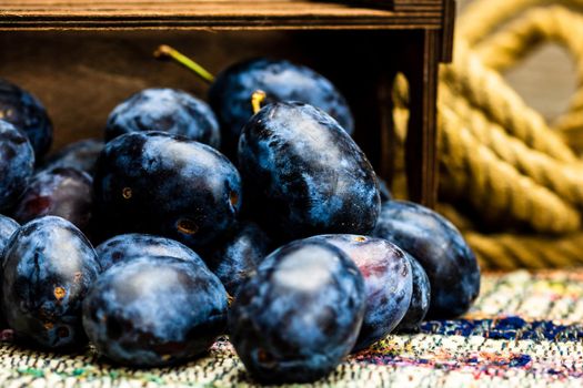 Ripe blue plums in a wooden crate in a rustic composition.