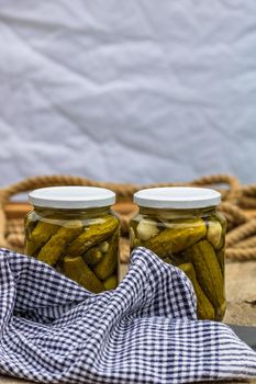 Glass jars with pickled red bell peppers and pickled cucumbers (pickles) isolated. Jars with variety of pickled vegetables. Preserved food concept in a rustic composition.