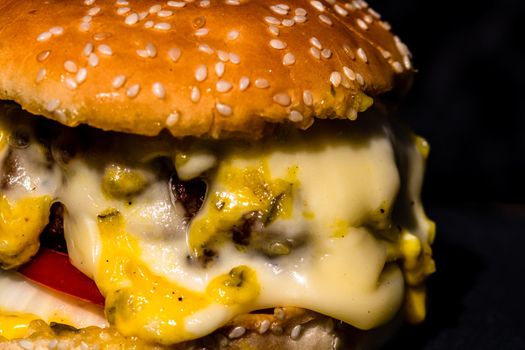 Detail of beef cheeseburger with melted cheese isolated on black background.