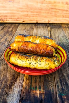 Sausages baked in dough sprinkled with salt and poppy seeds in a colorful plate. Sausages rolls, delicious homemade pastries in a rustic composition.