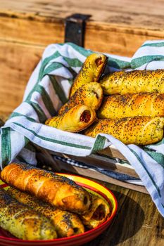 Sausages baked in dough sprinkled with salt and poppy seeds in a rustic composition. Sausages rolls, delicious homemade pastries.