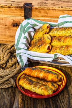 Sausages baked in dough sprinkled with salt and poppy seeds in a rustic composition. Sausages rolls, delicious homemade pastries.