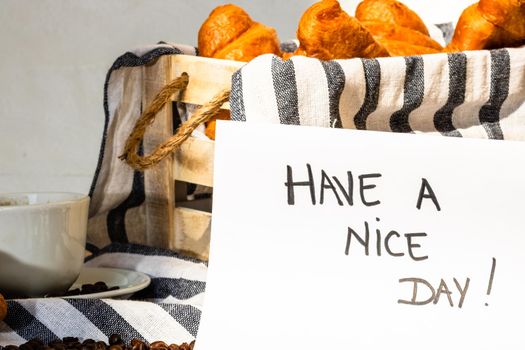 Coffee cup and buttered fresh French croissant on wooden crate. Food and breakfast concept. Morning message “have a nice day” on white board