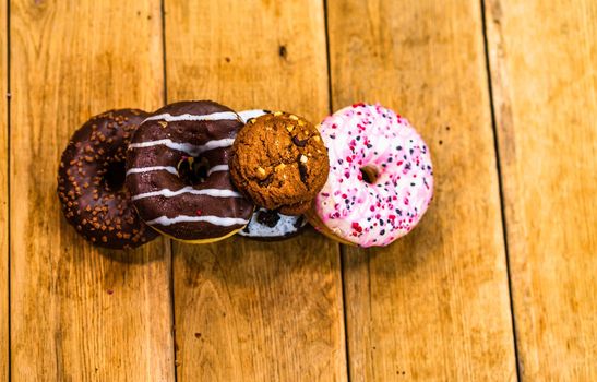 Colorful donuts on wooden table. Sweet icing sugar food with glazed sprinkles, doughnut with chocolate frosting. Top view with copy space