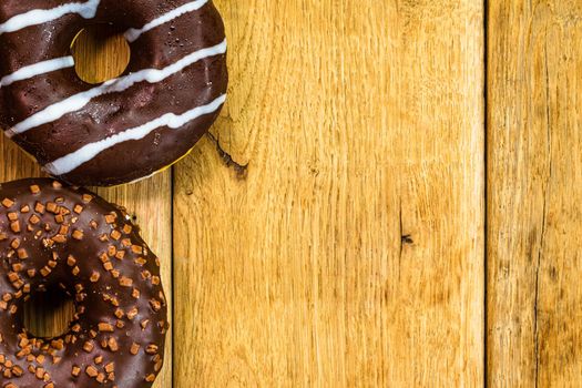 Colorful donuts on wooden table. Sweet icing sugar food with glazed sprinkles, doughnut with chocolate frosting. Top view with copy space