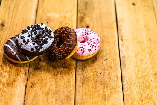 Colorful donuts on wooden table. Sweet icing sugar food with glazed sprinkles, doughnut with chocolate frosting. Top view with copy space