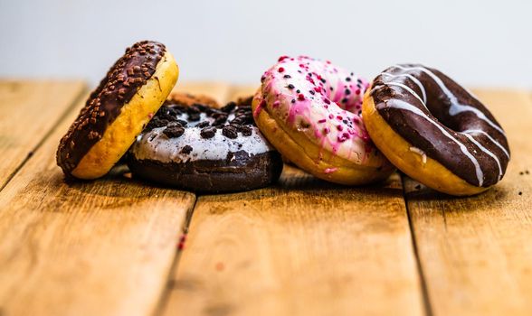 Colorful donuts on wooden table. Sweet icing sugar food with glazed sprinkles, doughnut with chocolate frosting. Top view with copy space