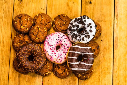 Colorful donuts on wooden table. Sweet icing sugar food with glazed sprinkles, doughnut with chocolate frosting. Top view with copy space