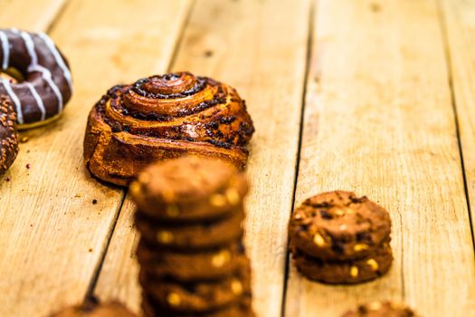 Colorful donuts, puff pastry and biscuits on wooden table. Sweet icing sugar food with glazed sprinkles, doughnut with chocolate frosting. Top view with copy space