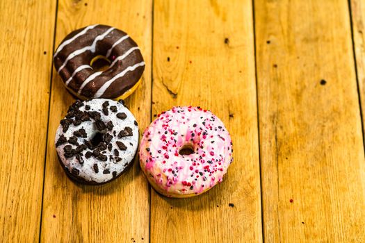 Colorful donuts on wooden table. Sweet icing sugar food with glazed sprinkles, doughnut with chocolate frosting. Top view with copy space