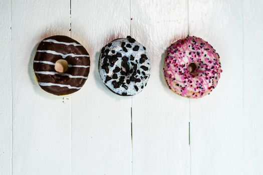 Colorful donuts on white wooden table. Sweet icing sugar food with glazed sprinkles, doughnut with frosting. Top view with copy space