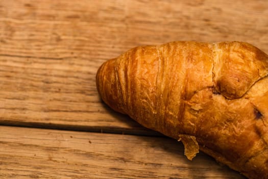 Detail of fresh croissant on wooden table. Food and breakfast concept. Top view and copy space