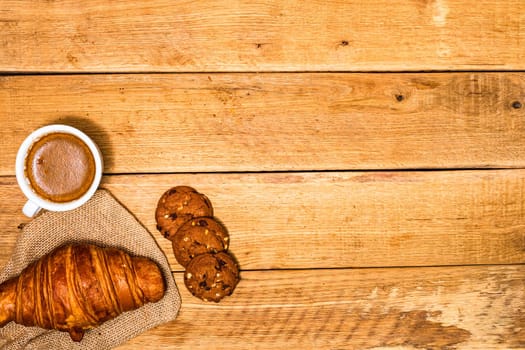 Fresh croissant and biscuits on wooden table. Coffee, food and breakfast concept. Desserts, fresh pastries and coffee. Top view and copy space