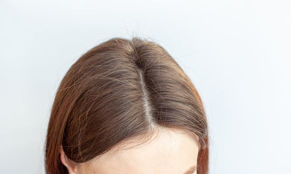 A woman's head with a parting of gray hair that has grown roots due to quarantine. Brown hair on a woman's head close-up.