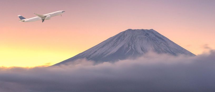 Commercial airplane flying over beautiful natural landscape view of Mount Fuji during sunrise in winter season at Japan. Elegant Design with copy space for travel concept.