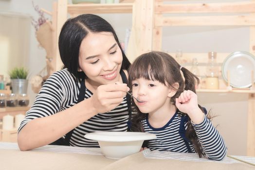 Happy family of asian mom feeding healthy breakfast to her cute daughter in the morning. Photo series of family, kids and happy people concept.