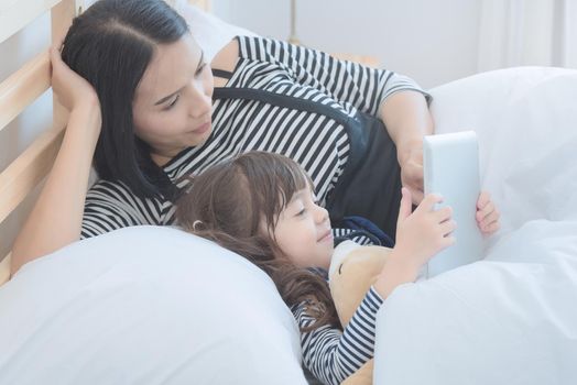 Happy loving family, asian young mother watching cartoon on smart tablet with her daughter in holiday. Photo design for family, kids and happy people concept.