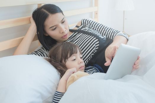 Happy loving family, asian young mother watching cartoon on smart tablet with her daughter in holiday. Photo design for family, kids and happy people concept.