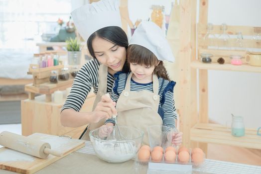 Asian mother and her daughter are preparing the dough to make a cake in the kitchen room on vacation.Photo series of Happy family concept.