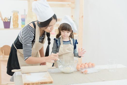 Asian mother and her daughter are preparing the dough to make a cake in the kitchen room on vacation.Photo series of Happy family concept.