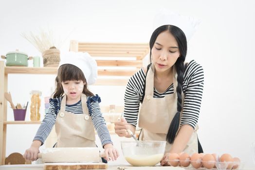 Asian mother and her daughter are preparing the dough to make a cake in the kitchen room on vacation.Photo series of Happy family concept.